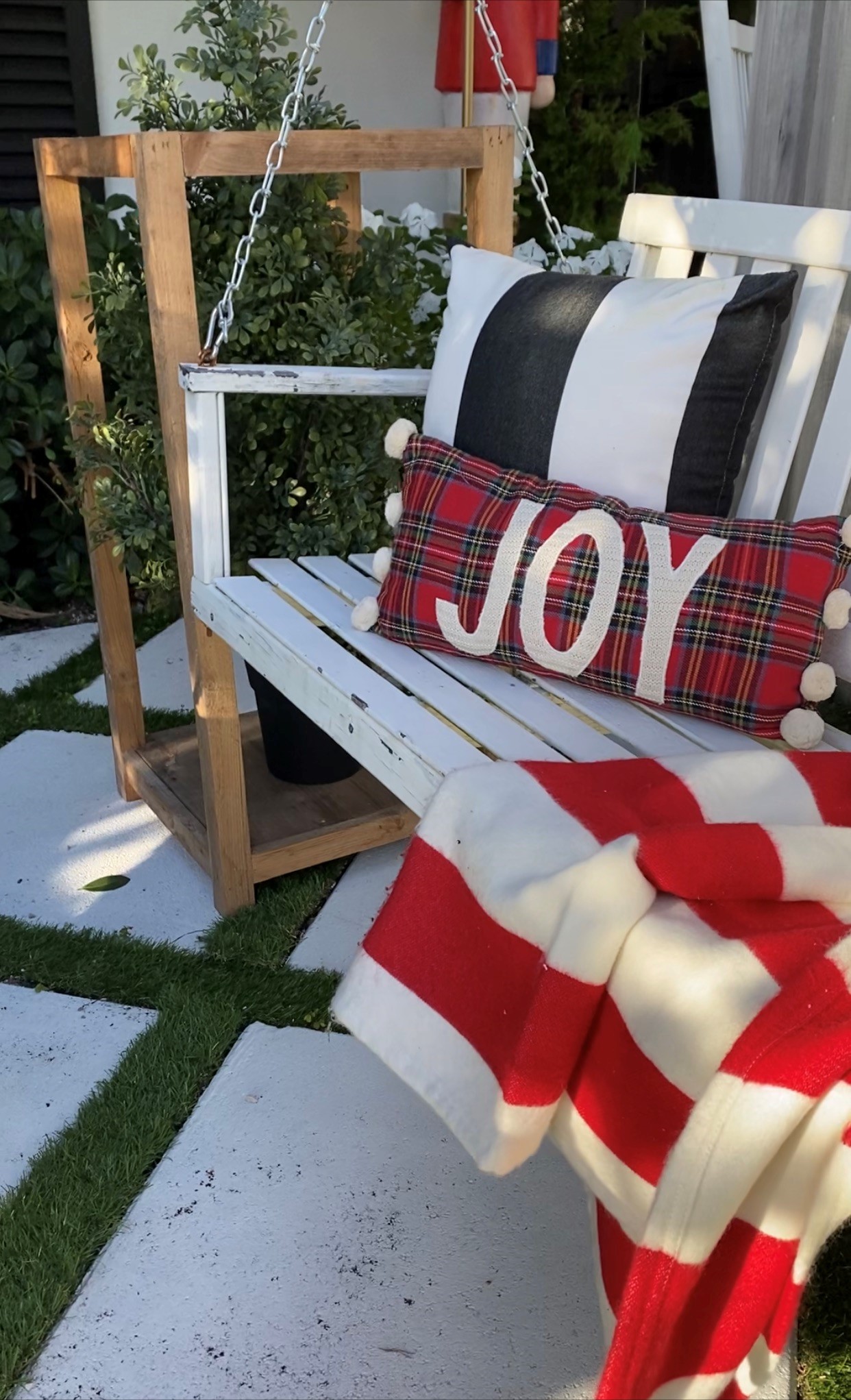 porch swing styled with Christmas pillows and a bright red throw blanket with a wooden lantern stand and Christmas tree inside