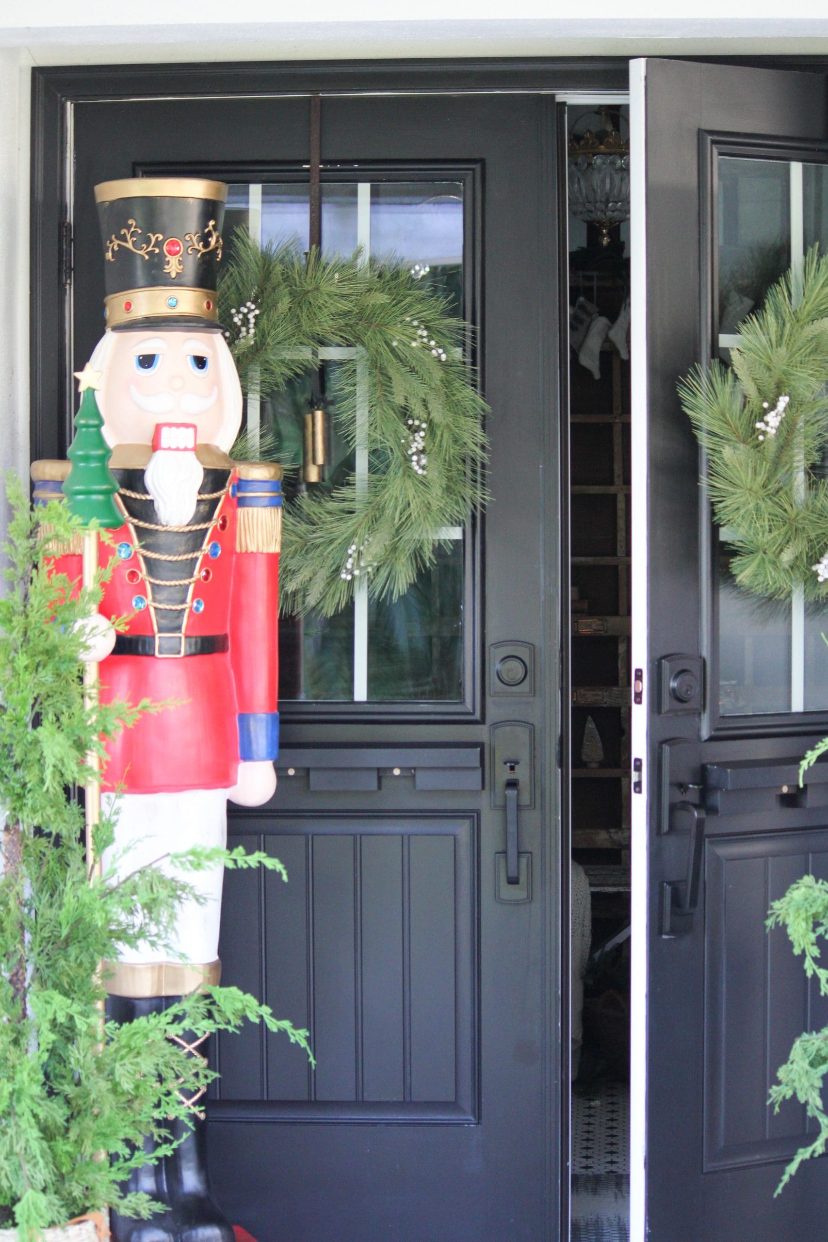 black front door with wreath on front door and large nutcracker beside it