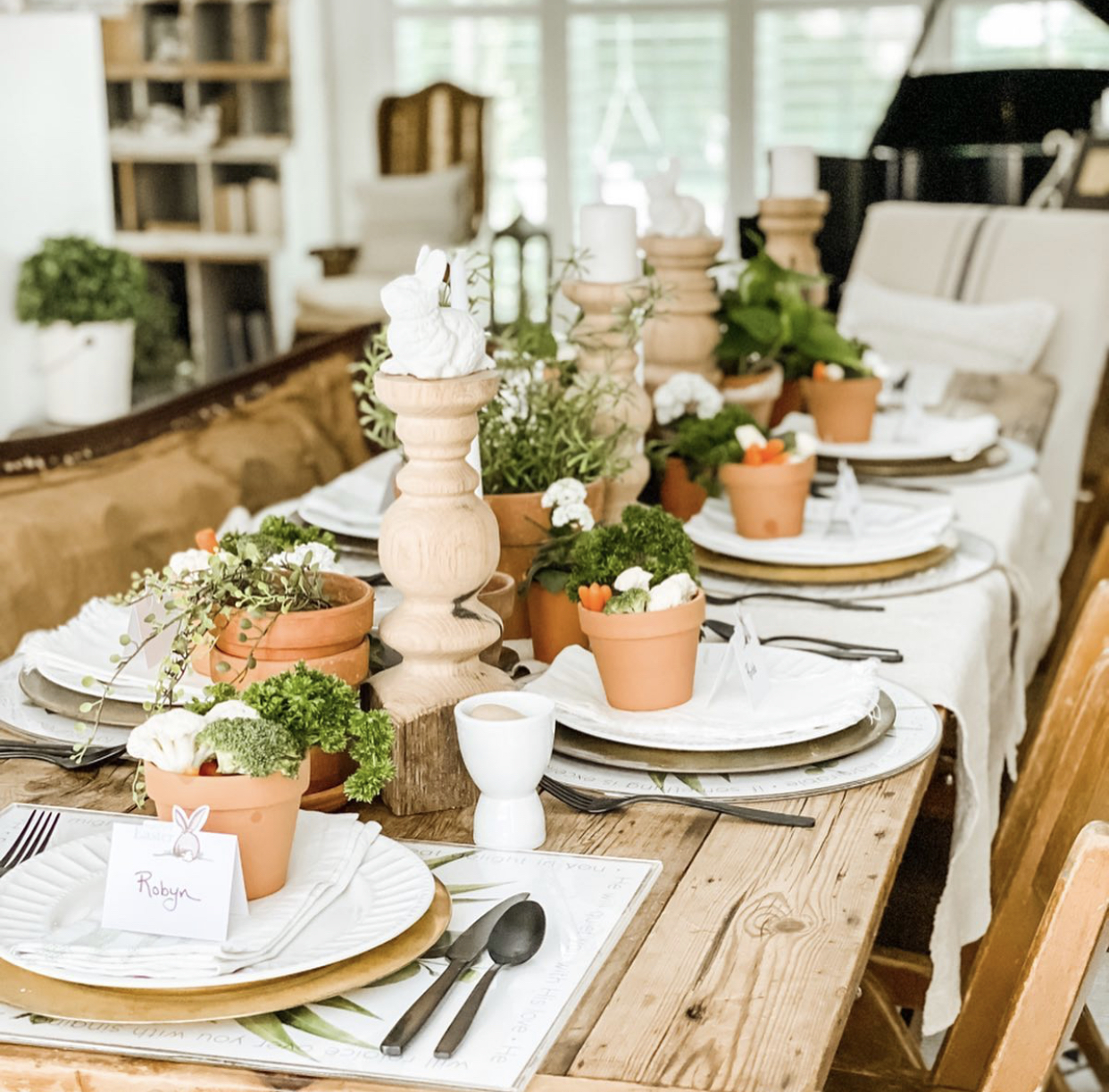 beautiful spring tablescape with greenery down the middle in terracotta pots and a small terracotta pot on each plate with veggies inside