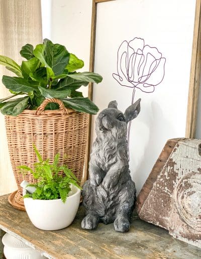 Original Art in frame behind wicker basket & plant with gray rabbit in between