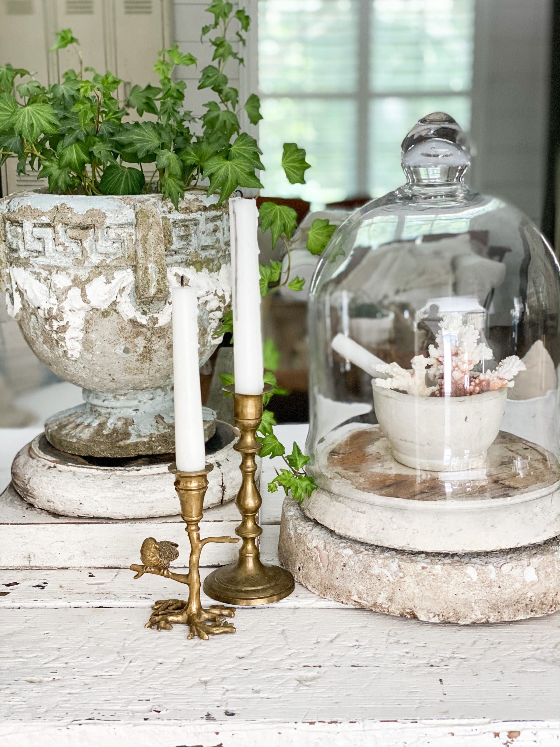 a glass cloche with a mortar and pestle filled with different corals next to summery brass candlesticks