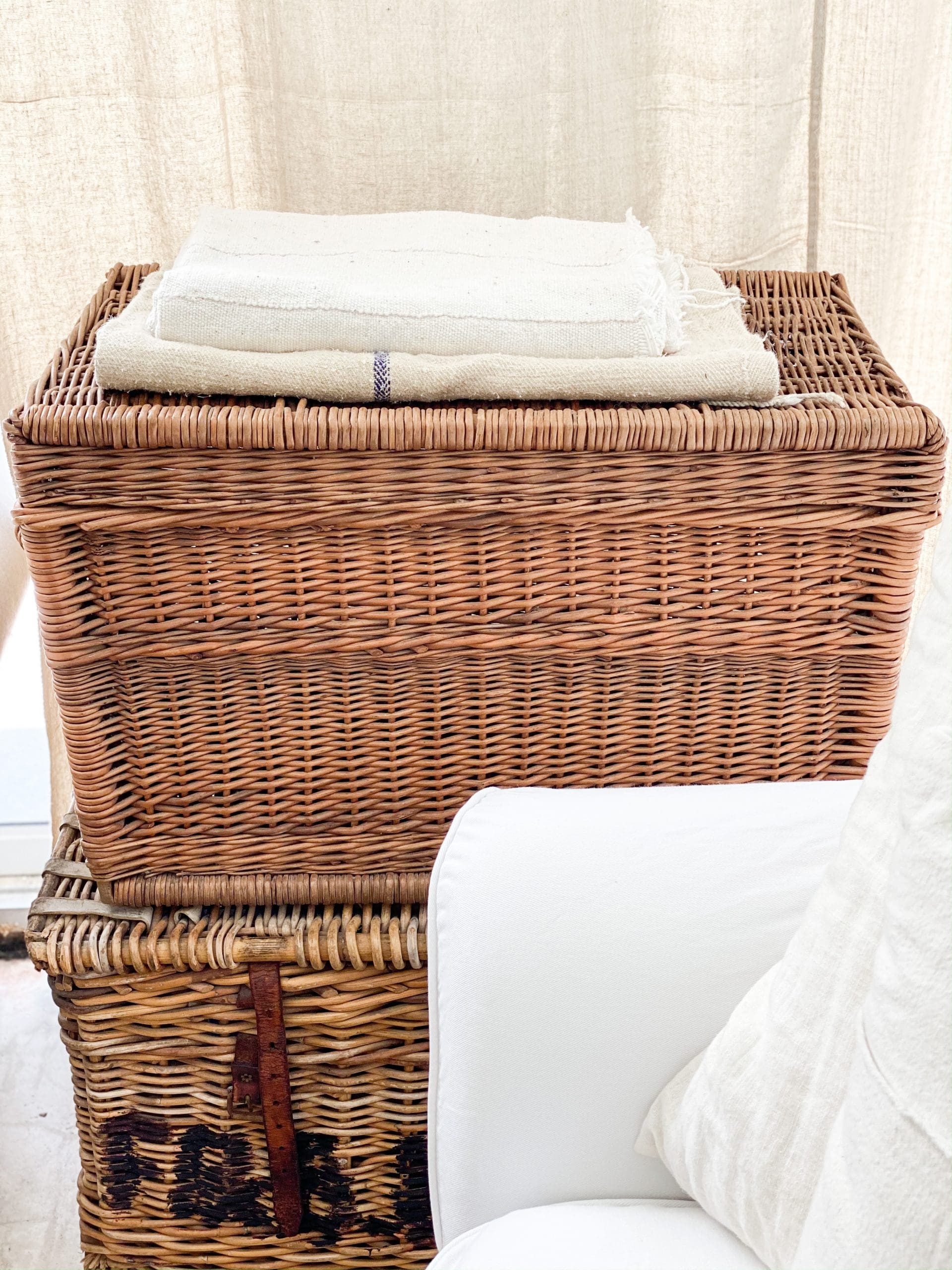 two large vintage woven baskets stacked on top of each other with cozy linen blankets folded on top