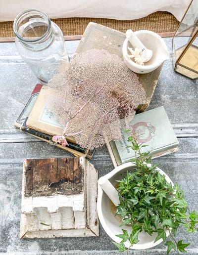 Coffee table decor: Old books, by white mortar & pestle & white architectural salvage. A small white mortar & pestle sits on an old brown reference volume.