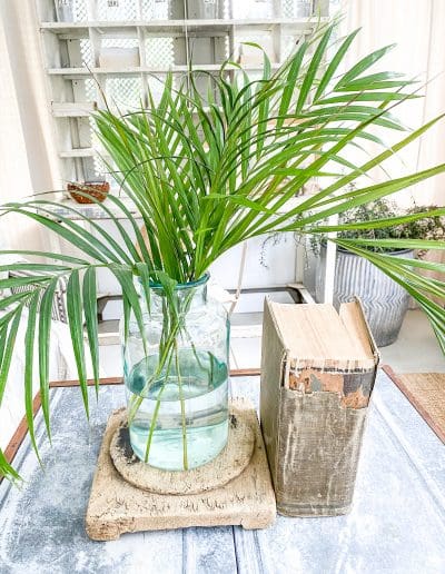 Zinc top coffee table with salvage riser, green glass vase with palm fronds & vintage bound book.