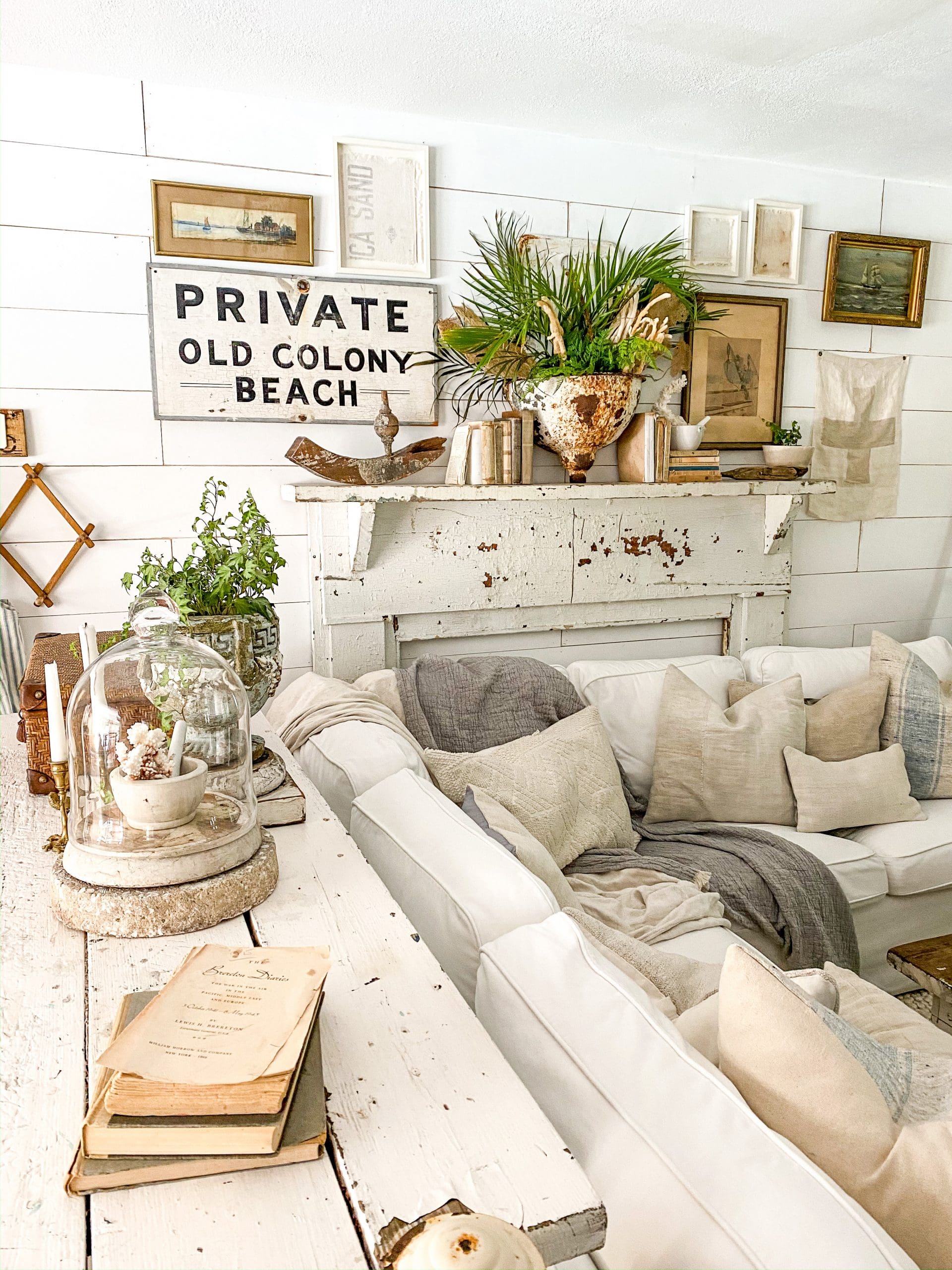 chippy white mantel styled for summer with a cozy white couch and coastal gallery wall