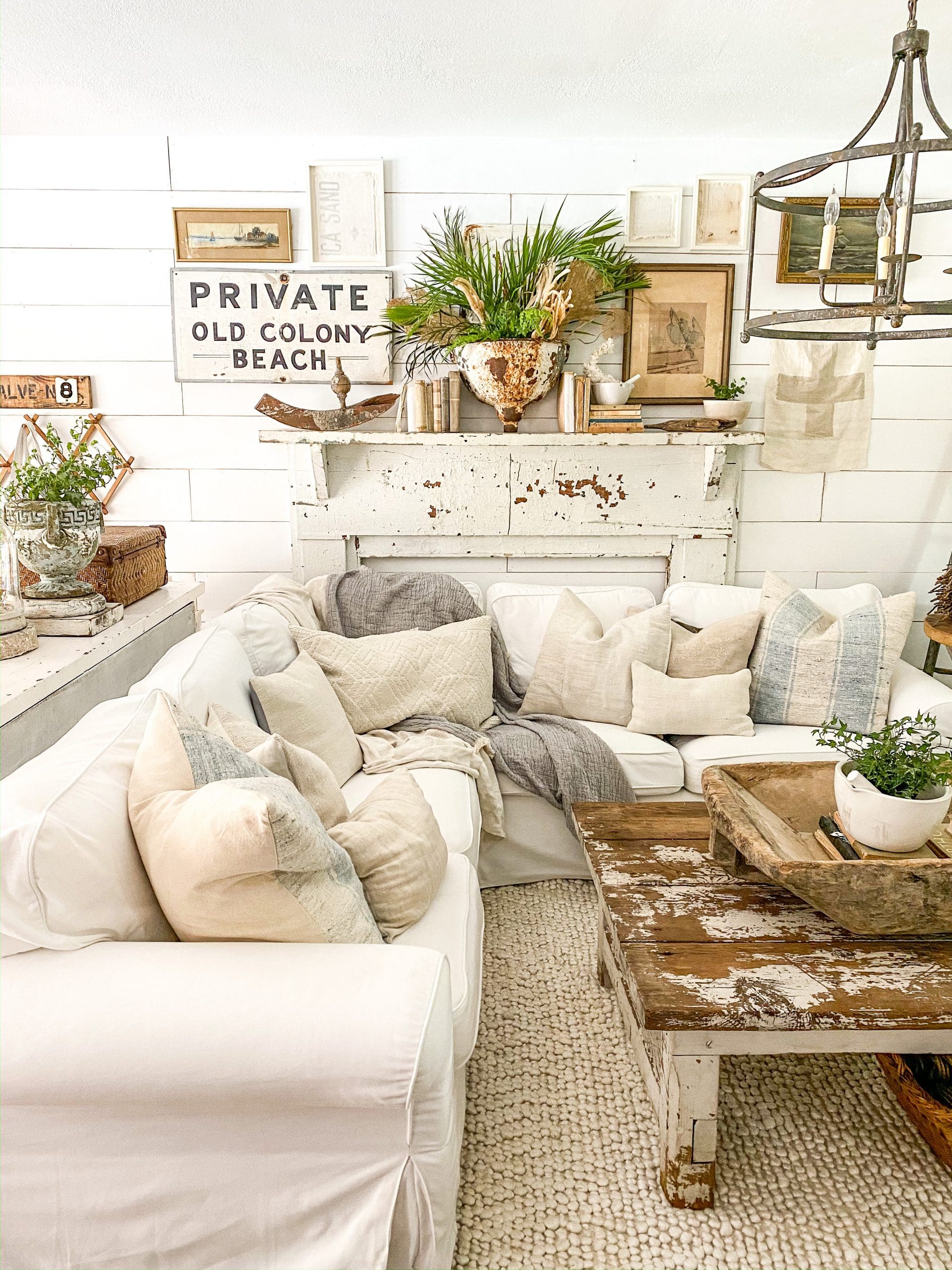 cozy white couch with chippy white mantel styled for summer and a coastal gallery wall behind it