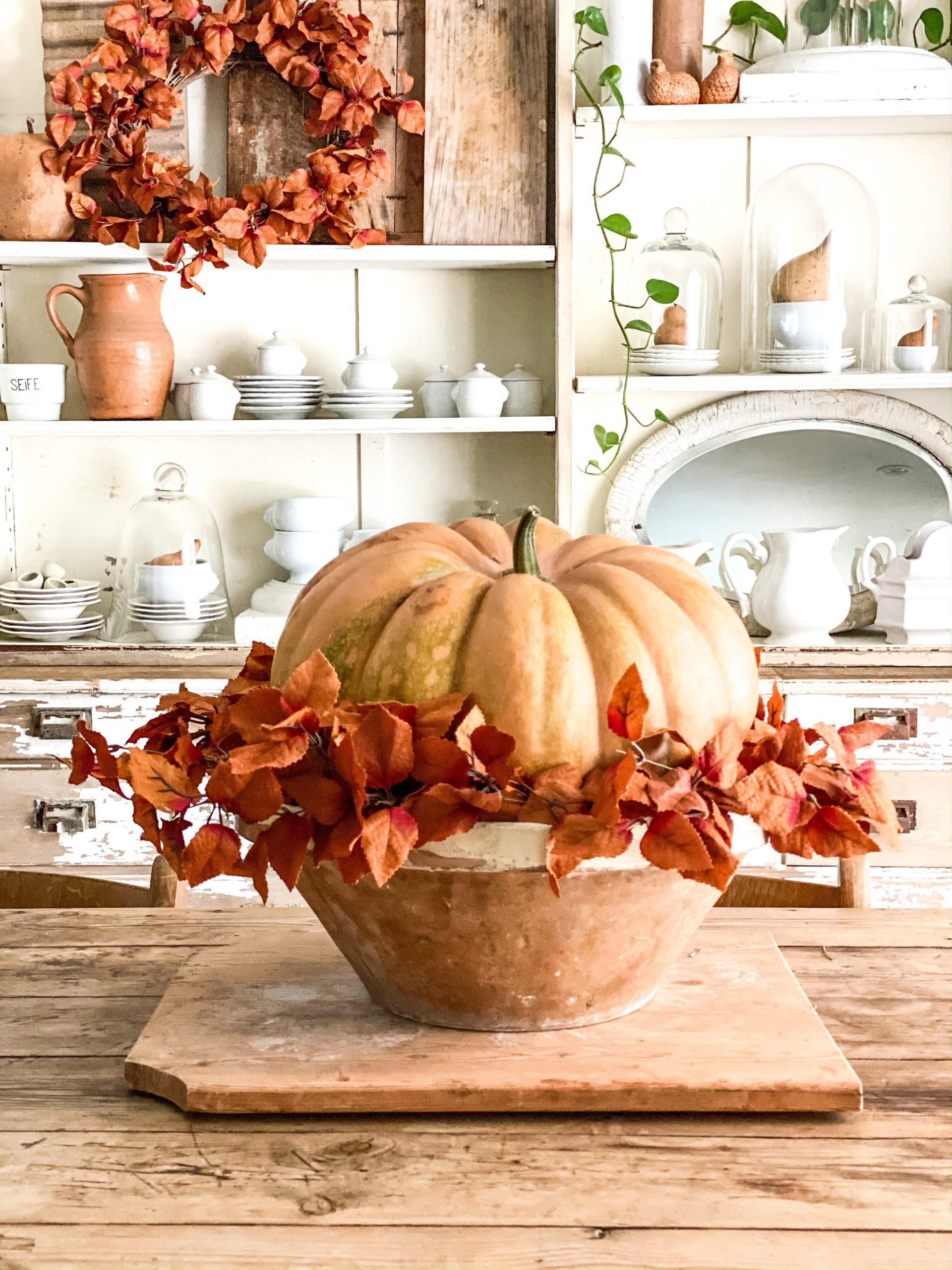 large orange pumpkin in a large bowl with fall greenery
