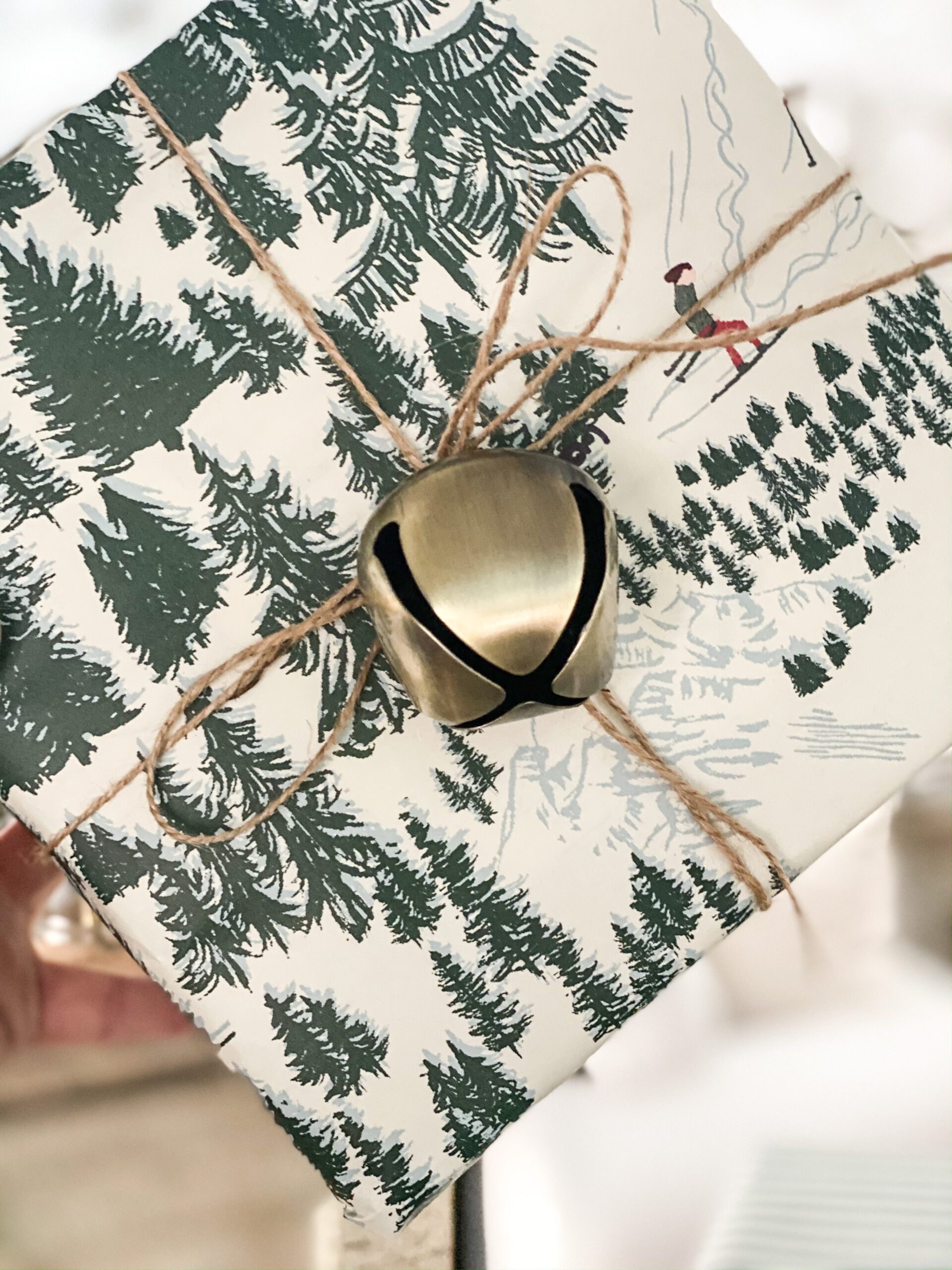 christmas tree wrapping paper with a gold bell tied to it with twine