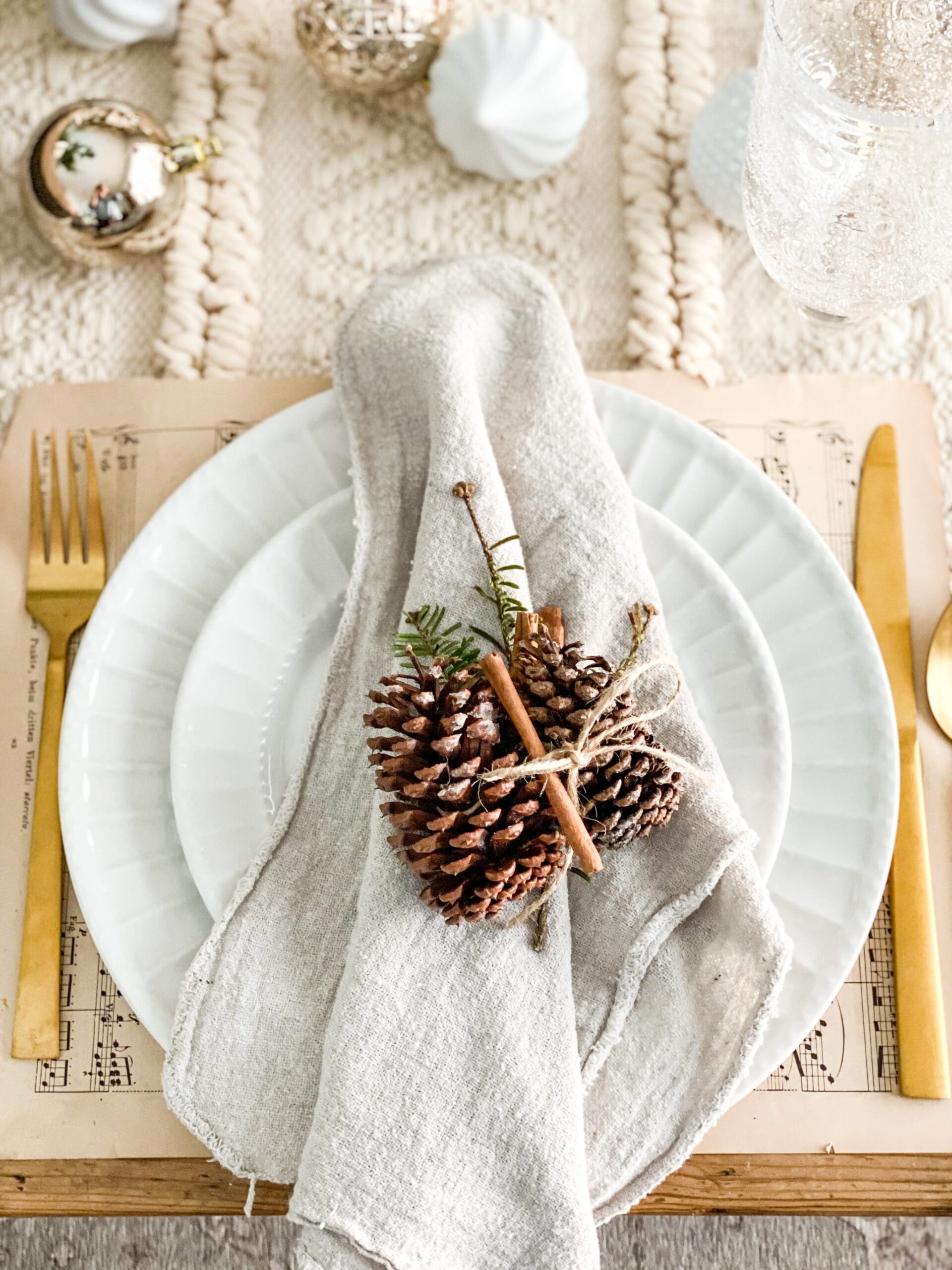 two pinecones and a sprig of Christmas greenery tied around a napkin as a napkin ring