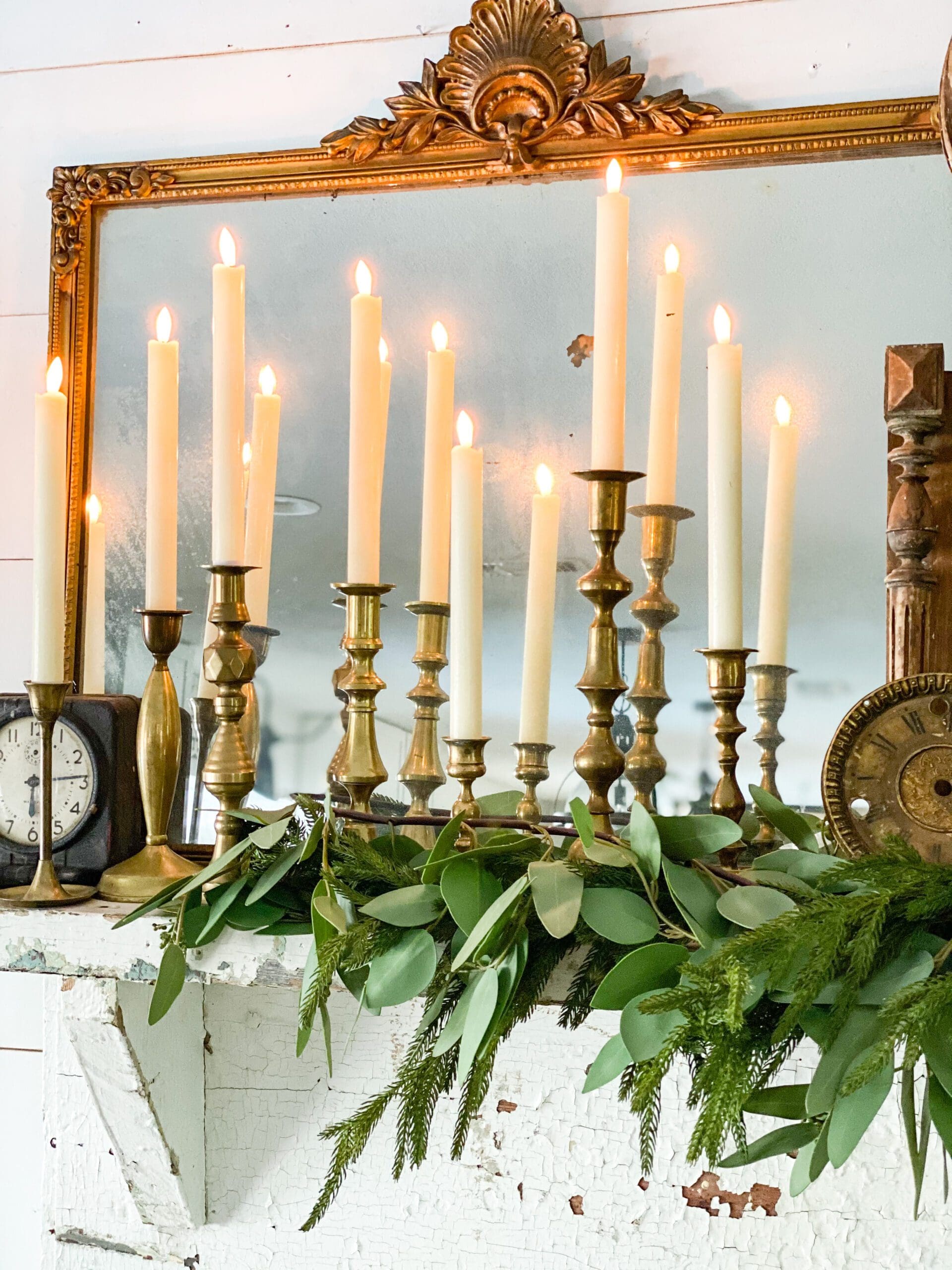 brass candlesticks holding flameless candles reflected in a vintage gold mirror