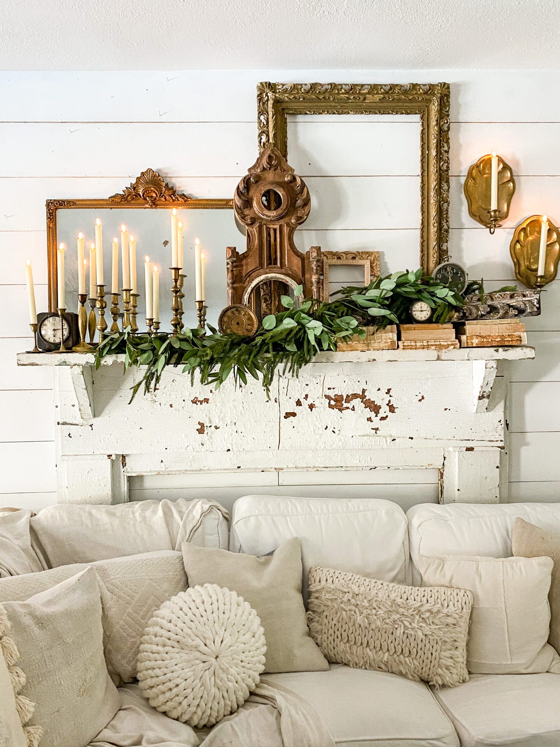 white mantel styled with brass candlesticks, faux greenery, and large wooden frames and mirrors