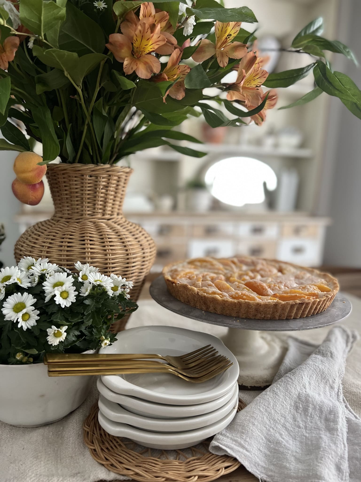 peach tart on a white cake stand with a small vase of white flowers beside it