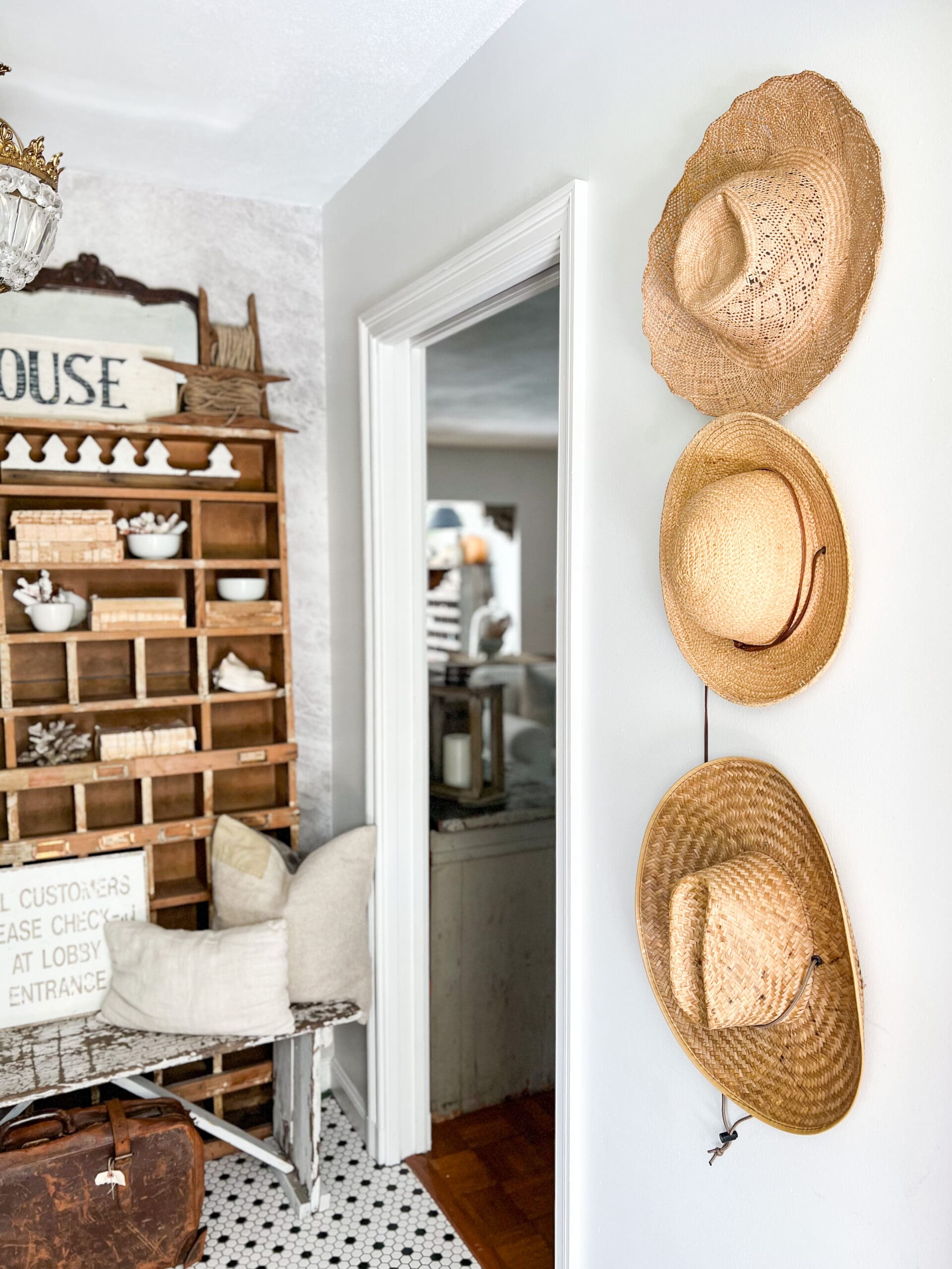 entryway with vintage straw hats hung on the wall and a chippy white bench in front of old wooden cubbies styled with pieces of coral