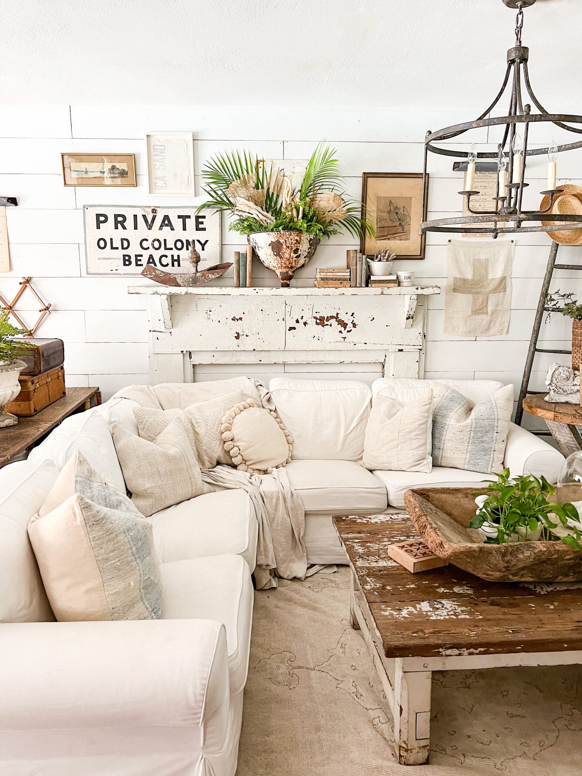 coastal living room styled with fresh summer greenery, old coastal signs and coral pieces, and vintage throw pillows on a white couch