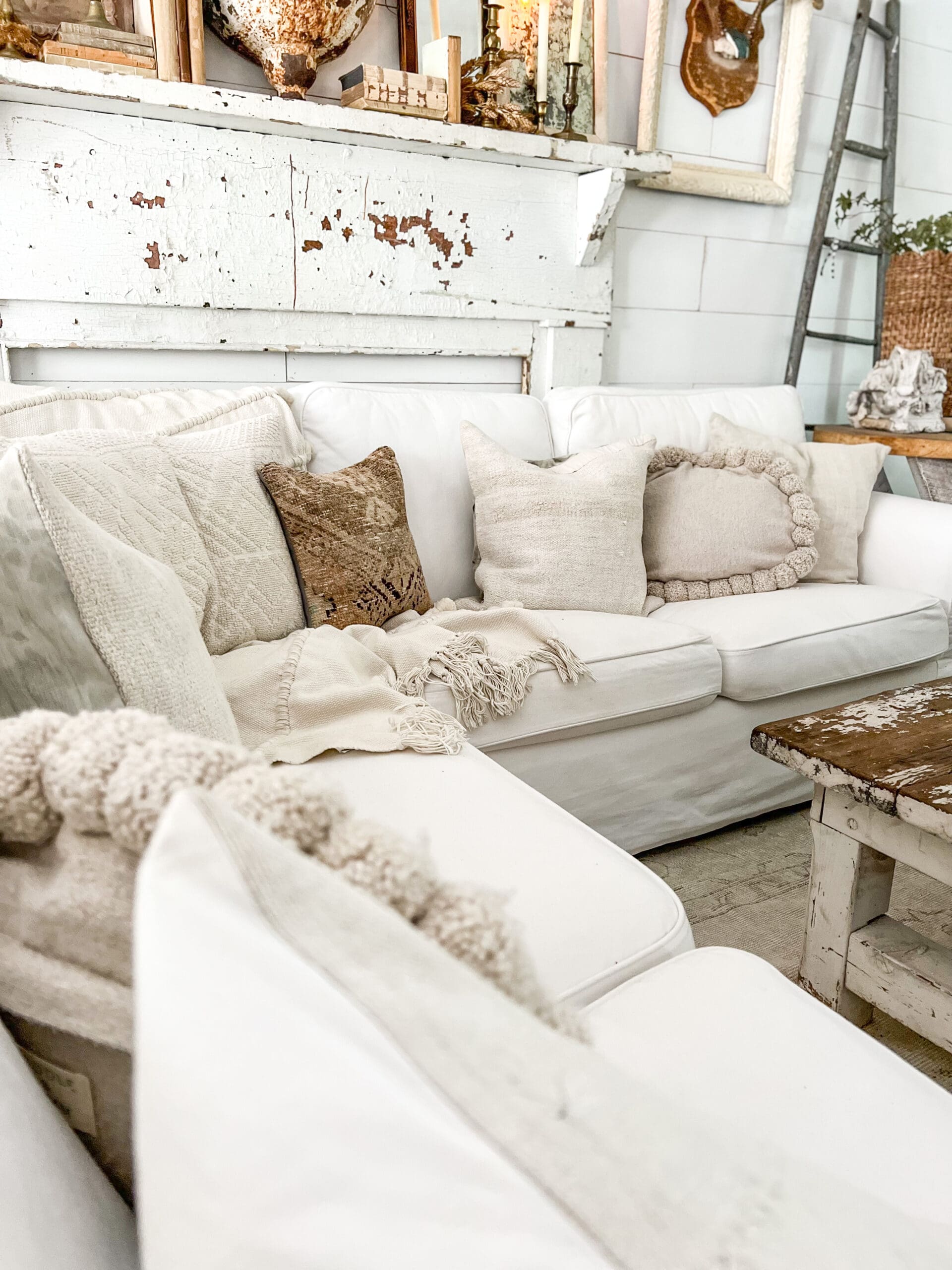 White sectional with neutral throw pillows and chippy white mantel