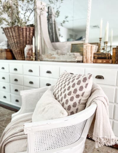 Patterned white pillow with smaller linen white pillow on a cotton throw in wicker white chair.