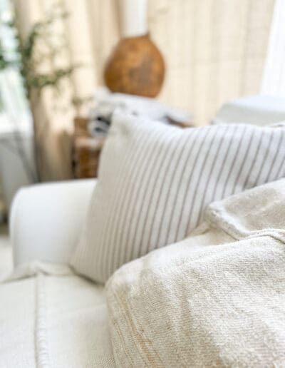 Creamy linen pillow on white couch, with striped square pillow in the background.