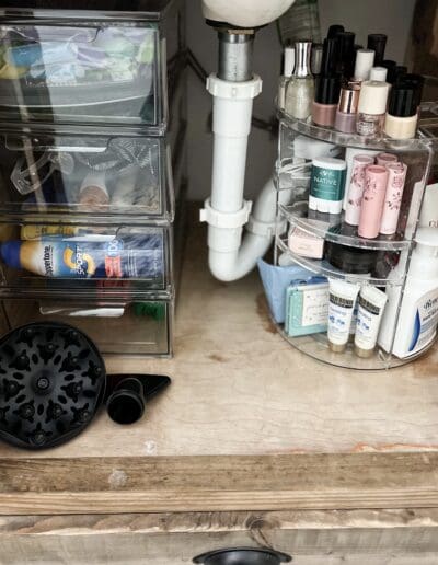 Plastic carousel & bins hold bathroom essentials neatly under on both sides of sink drain behind one open cabinet door.