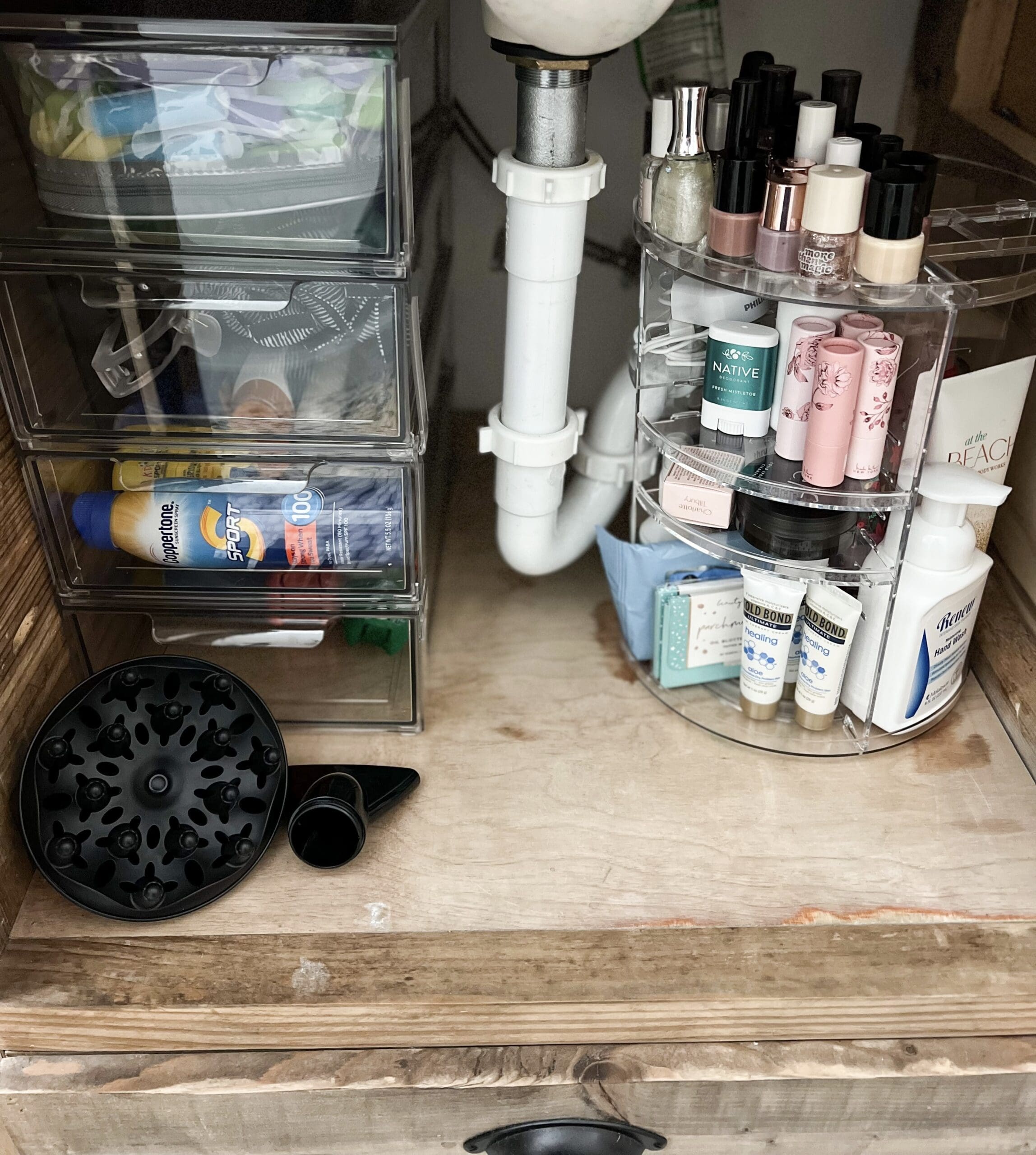 Plastic carousel & bins hold bathroom essentials neatly under on both sides of sink drain behind one open cabinet door.