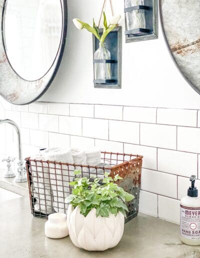Vintage locker basket with neatly rolled-up white handtowels sit on the cocrete countertop beside the chrome faucet & sink.
