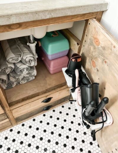 With cabinet door open, neatly rolled up gray and white pools towels are seen. Hair dryer and other accessories fit in a white holder screwed to the back of the cabinet door.