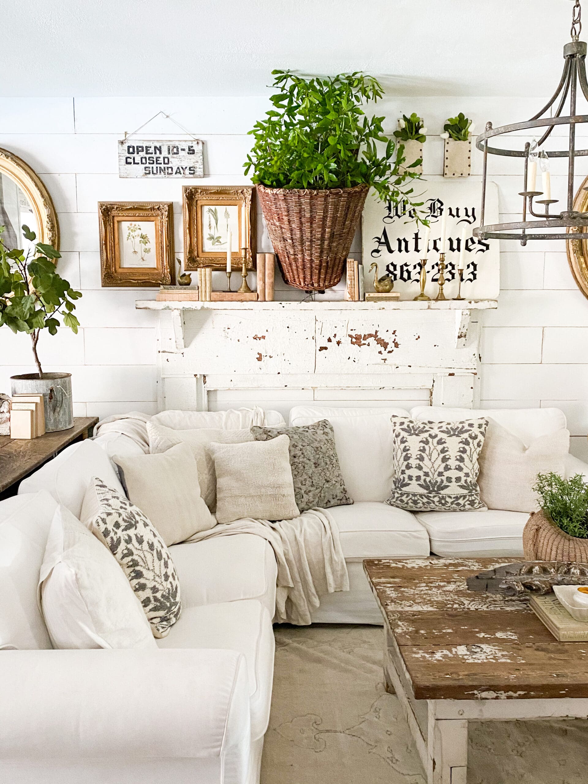 Wide view of family room with white sectional centered in front of vintage white mantel and black & white signs.