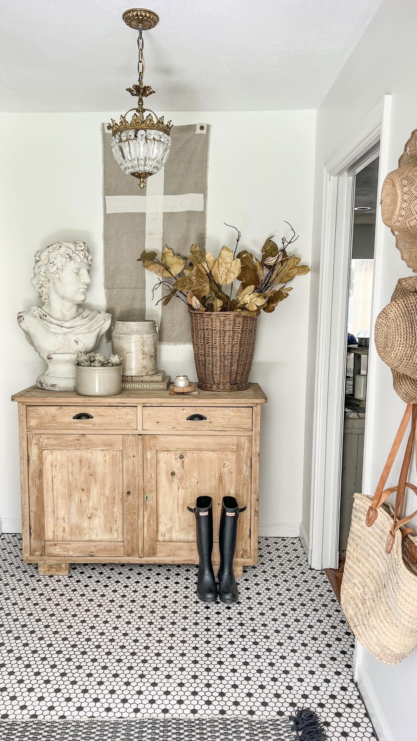 entryway cabinet with brown basket holding dried leaves, styled alongside a white concrete bust and white crocks