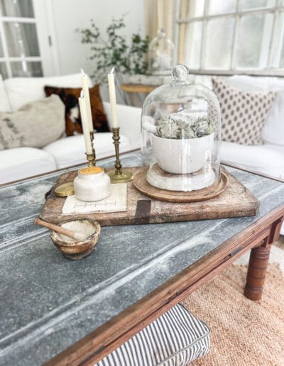 coffee table vignette styled with candlesticks, a candle, and a glass cloche above a mortar and pestle filled with faux artichokes