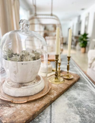 vignette styled with a wooden bread board and a mortar and pestle filled with artichokes under a glass cloche