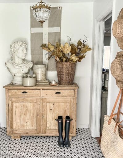 entryway styled with white concrete bust, woven basket with dried greenery, and white crocks