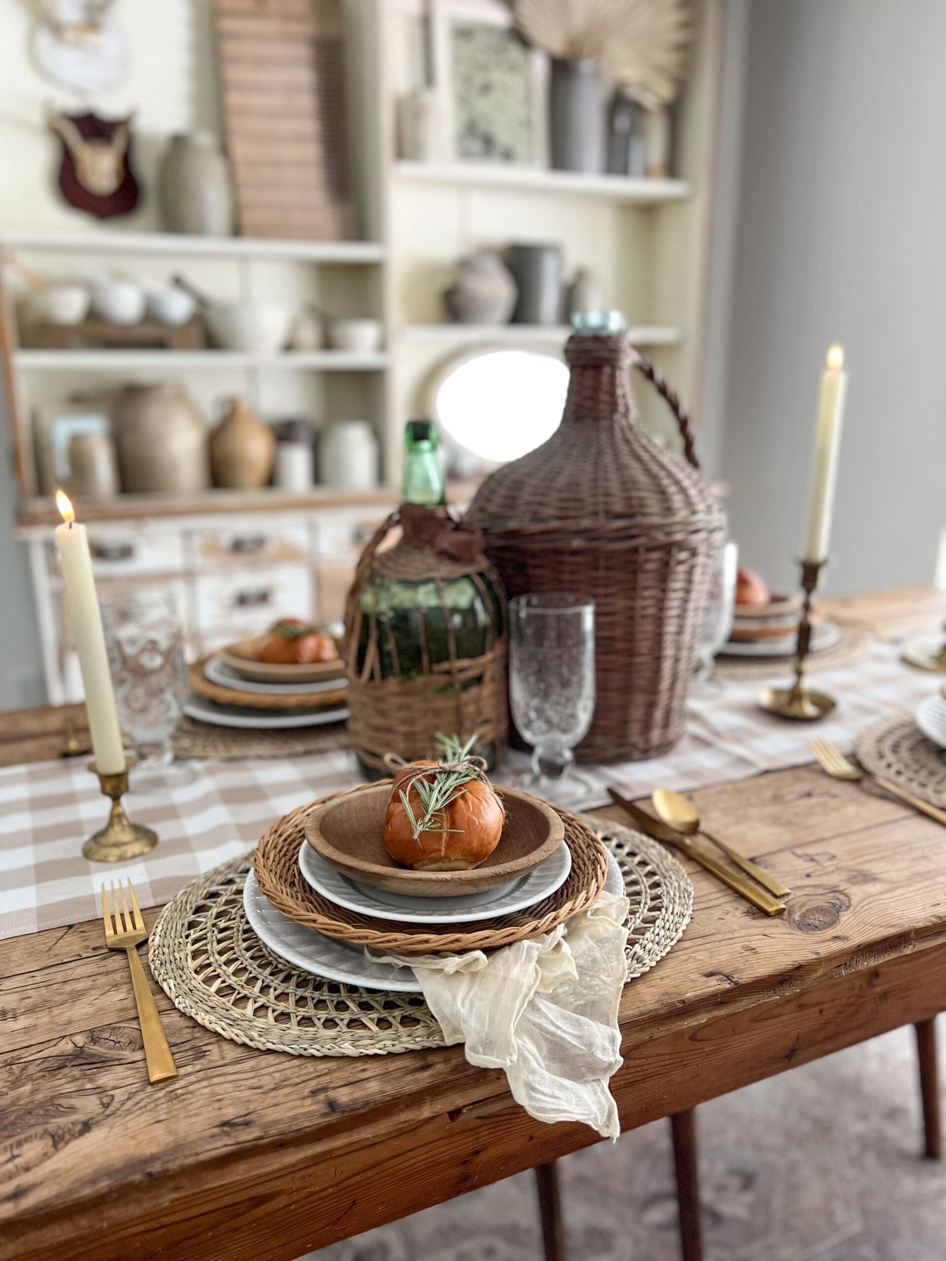tablescape featuring checkered table runner, gold candlesticks, and lots of woven texture