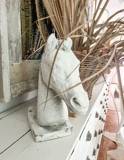 White concrete horse head styled next to a brown woven basket with dried greenery