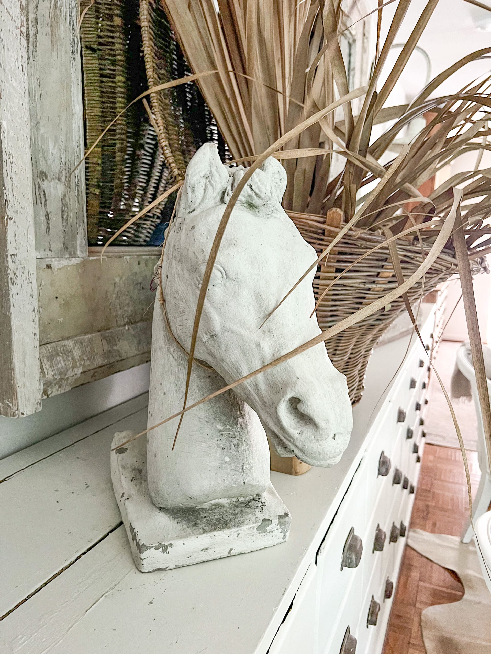 White concrete horse head styled next to a brown woven basket with dried greenery