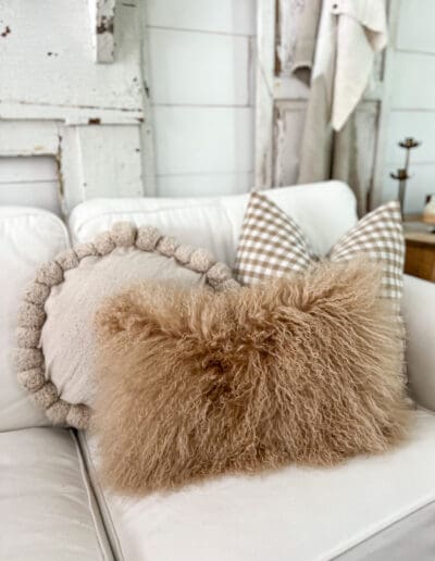 Fuzzy brown pillow on a white couch with a brown checkered pillow and a round pillow