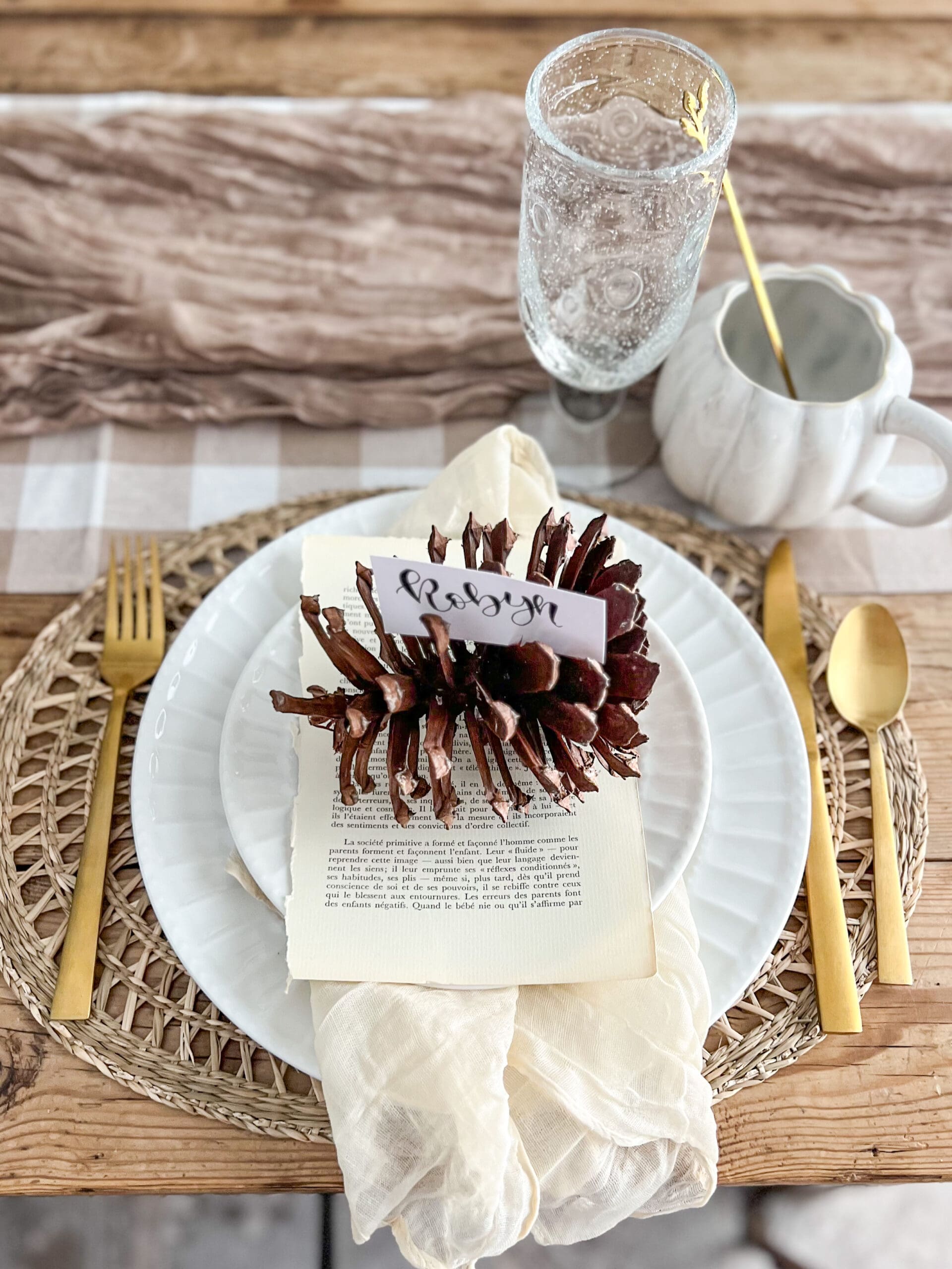 place setting with white dishes, a vintage book page, and a pinecone serving as a place card
