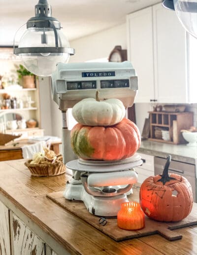 large white scale with two pumpkins stacked on top of it and a carved pumpkin next to it