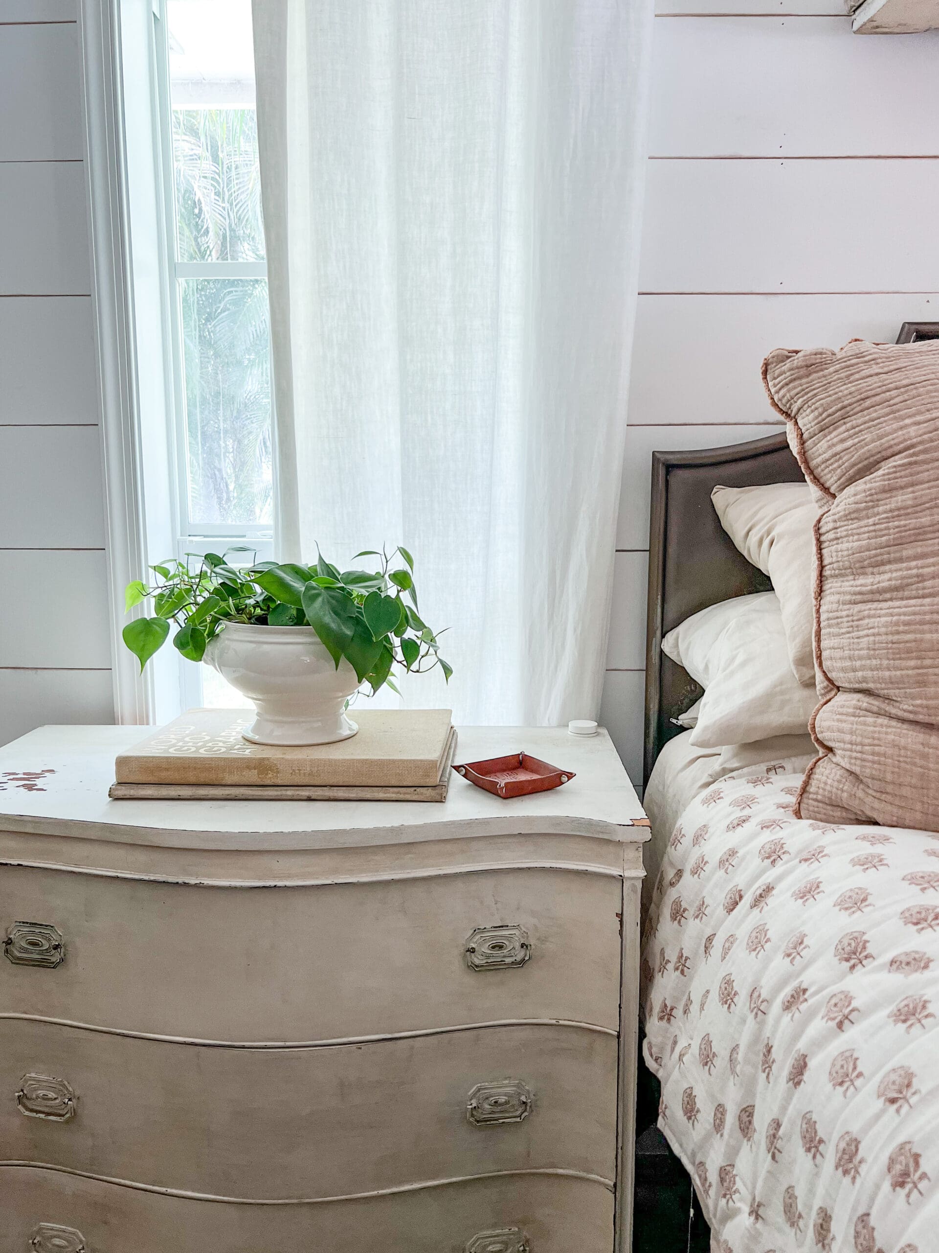 White nightstand styled with a large neutral colored book with an ironstone piece holding a plant on top