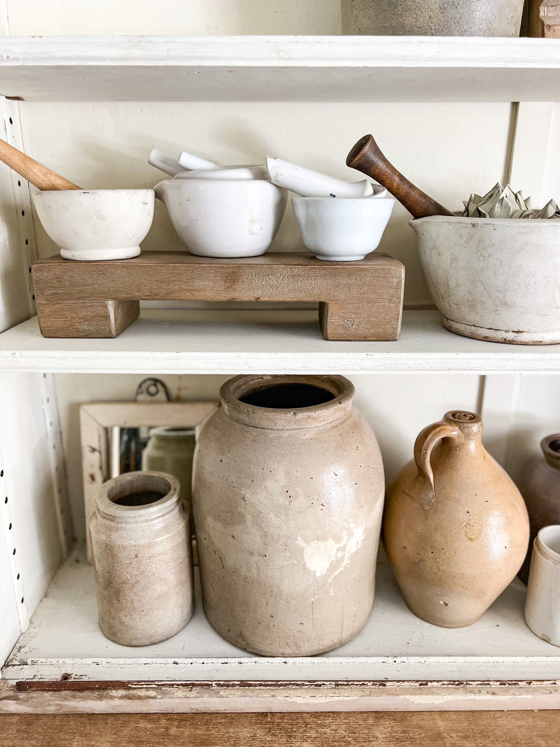 different sizes of crocks and mortar and pestles styled on apothecary shelves