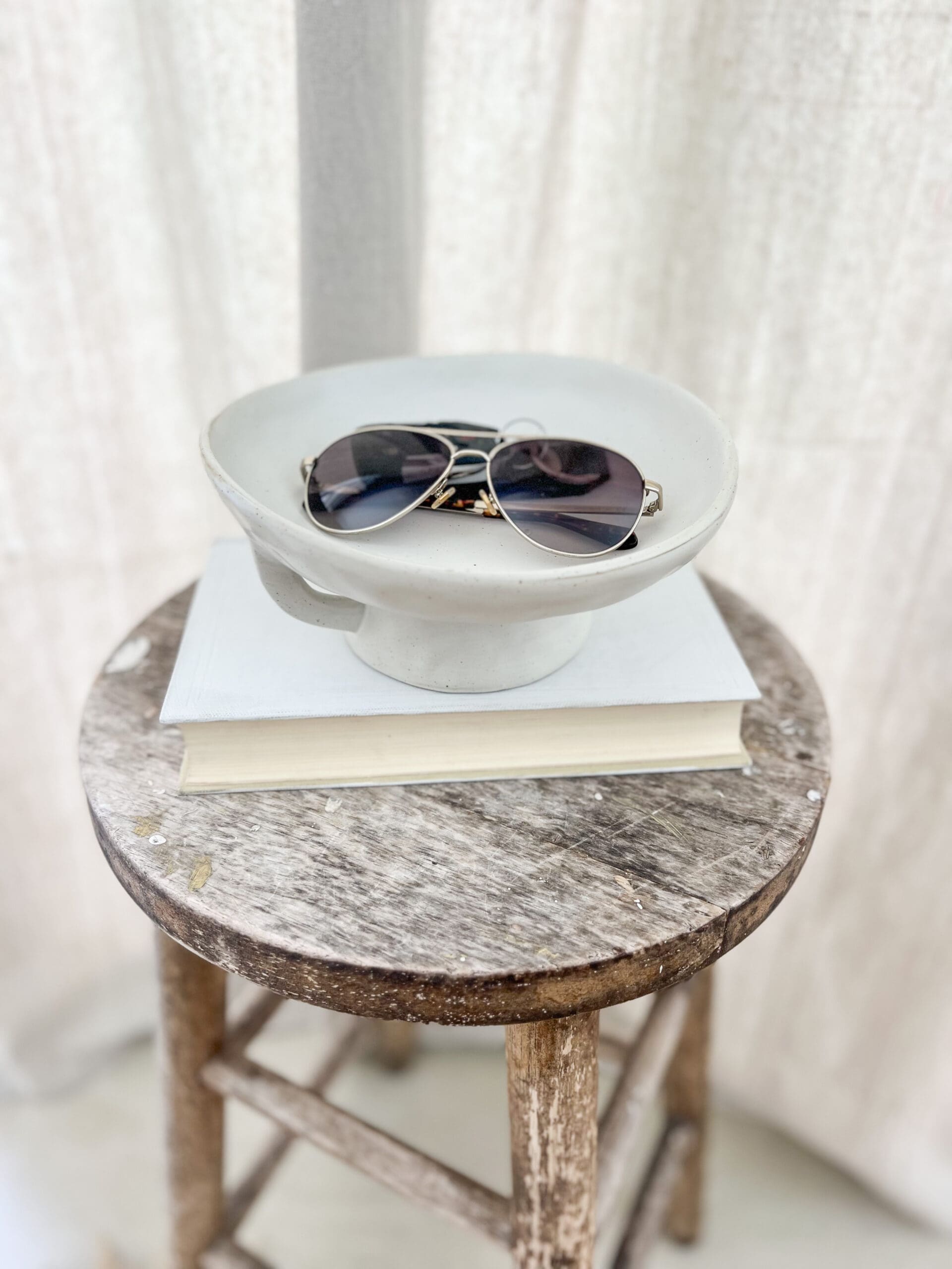 Pair of sunglasses in a white bowl on a wooden stool