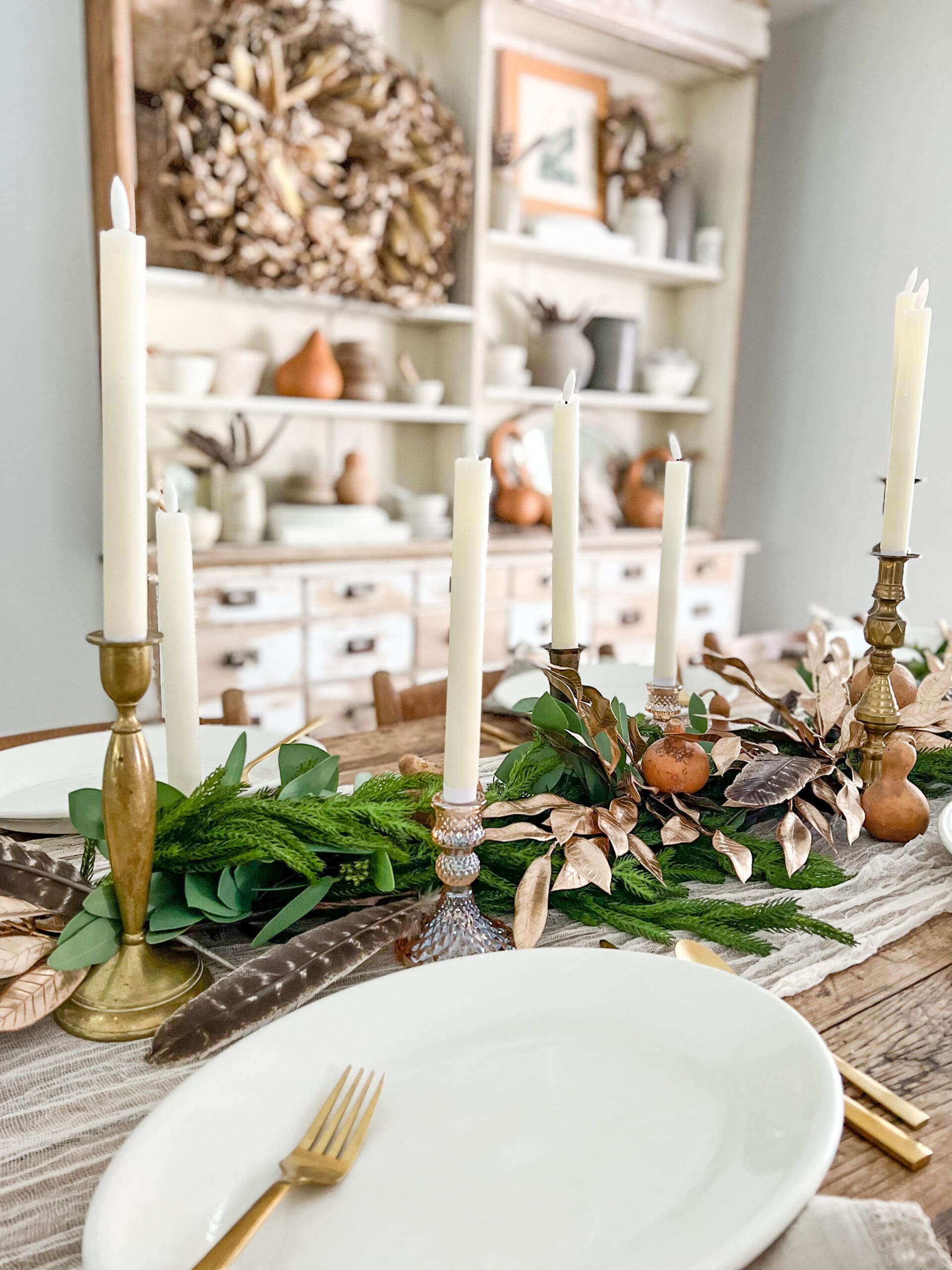 gold candlesticks and feathers tucked into green garland down the center of the table