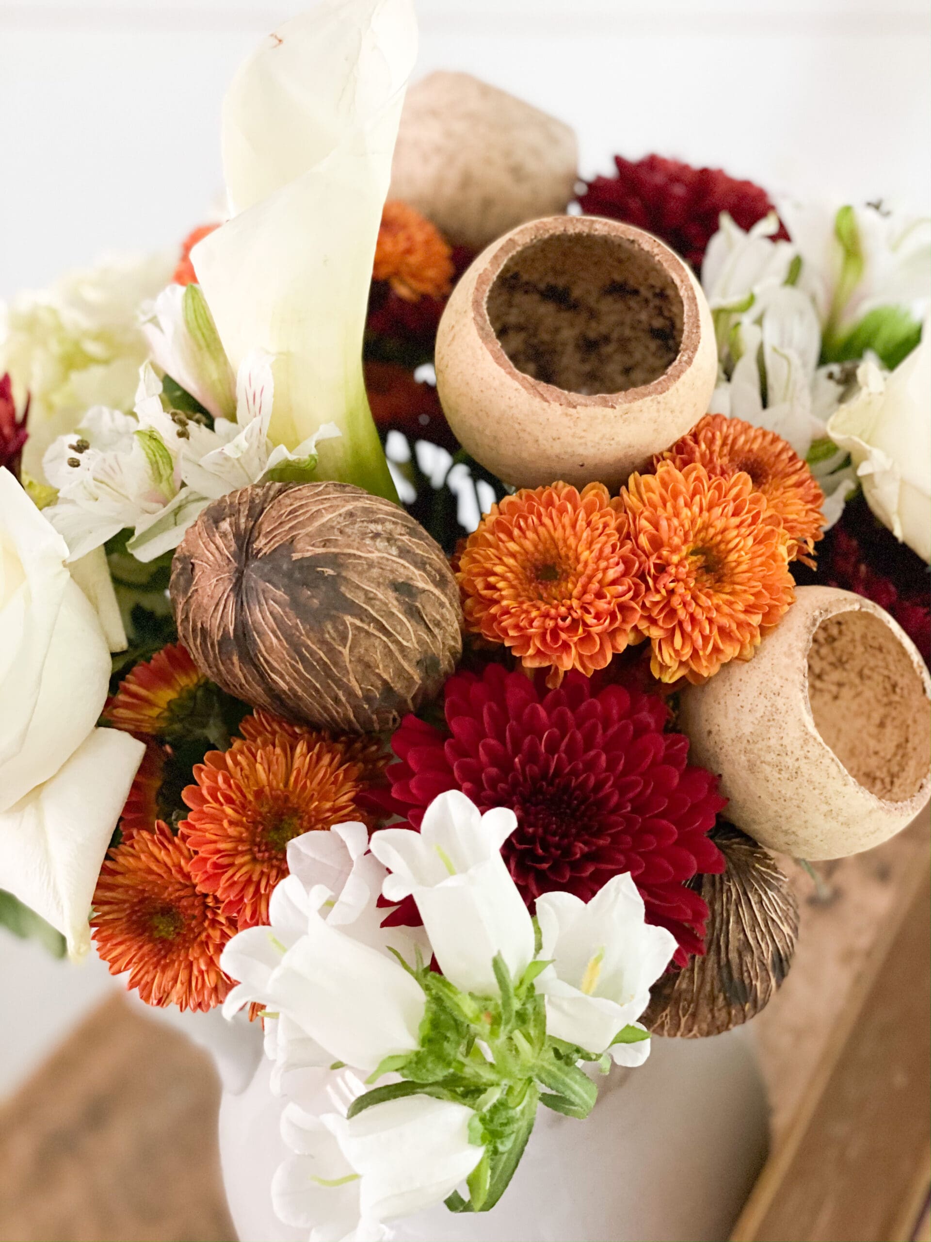 beautiful fall flower arrangement with vibrant red, orange, and white flowers and acorns