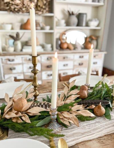 Gold candlesticks, greenery and faux gold greenery down the middle of a table, with feathers and gourds