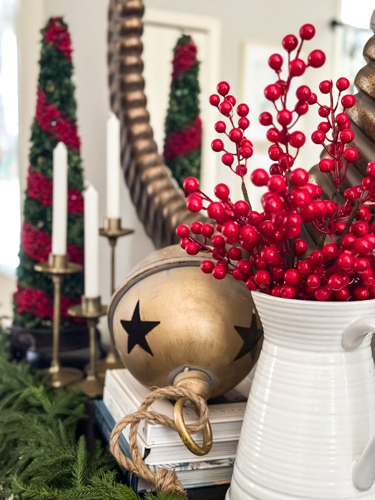 close up of a gold bell next to a white pitcher holding cranberry stems styled on an entryway table
