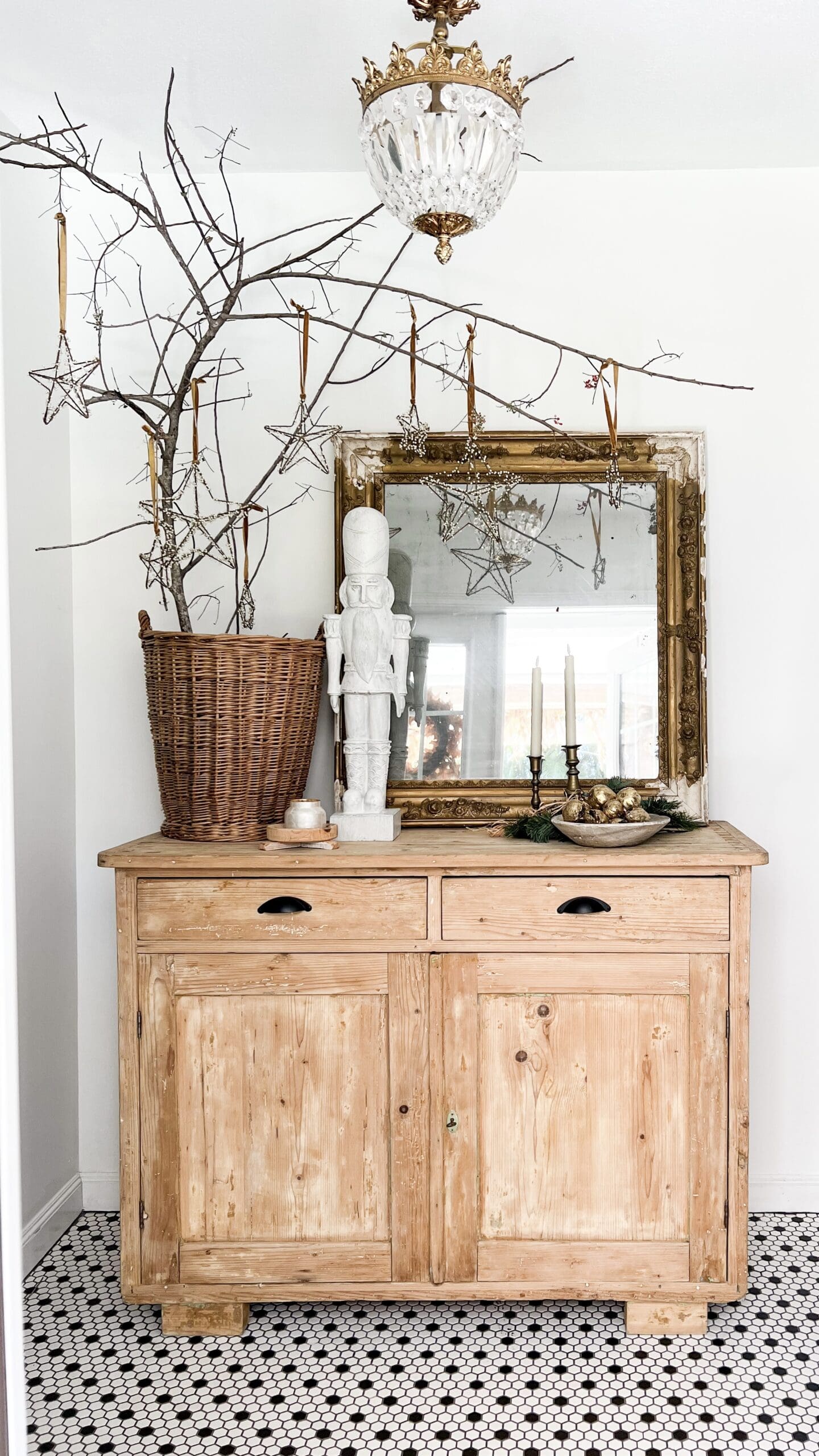 entryway styled with a large mirror, a large white nutcracker, and a large branch in a woven basket