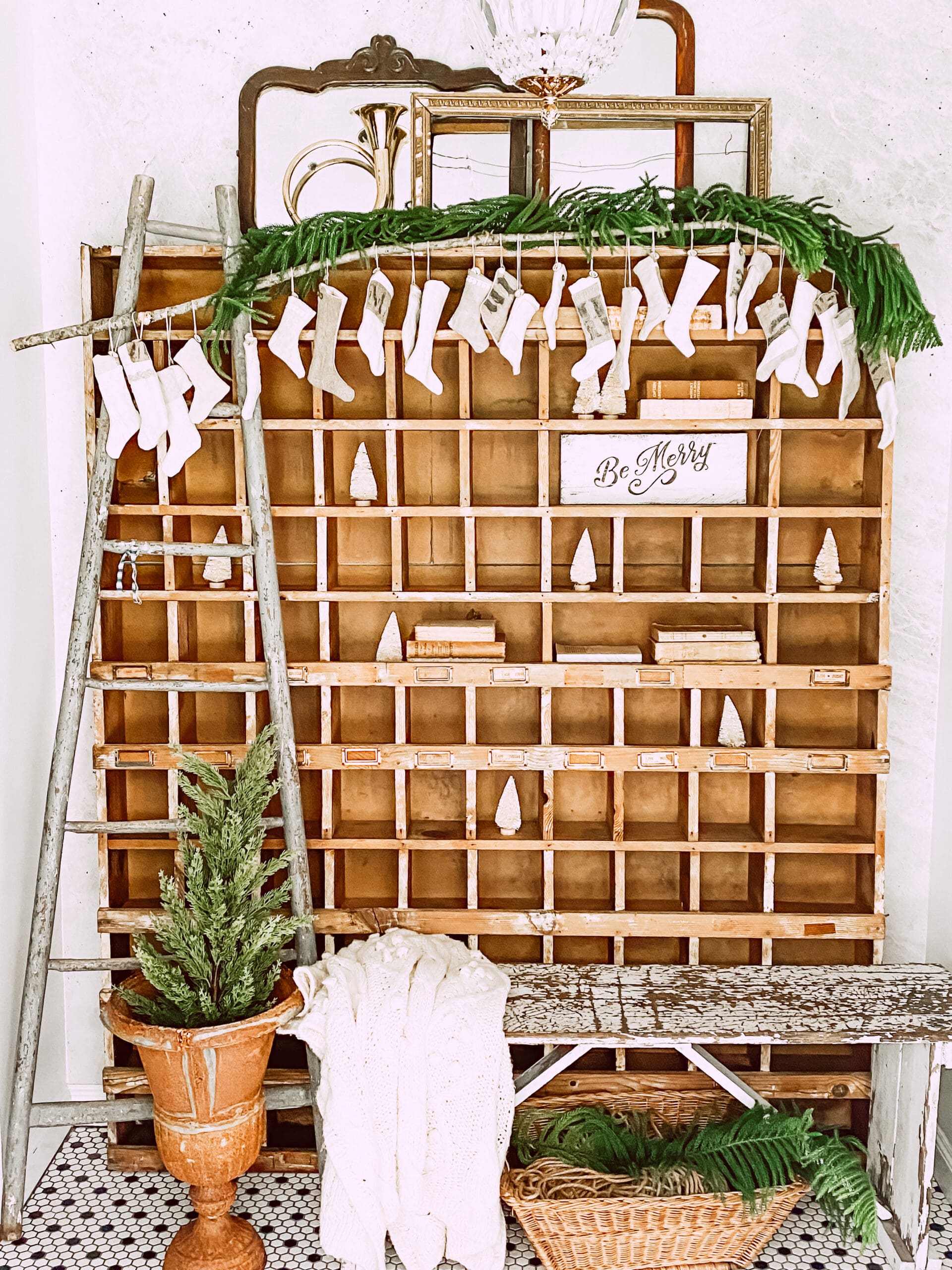 ladder leaning against wooden cubbies that are styled with stockings and Christmas greenery