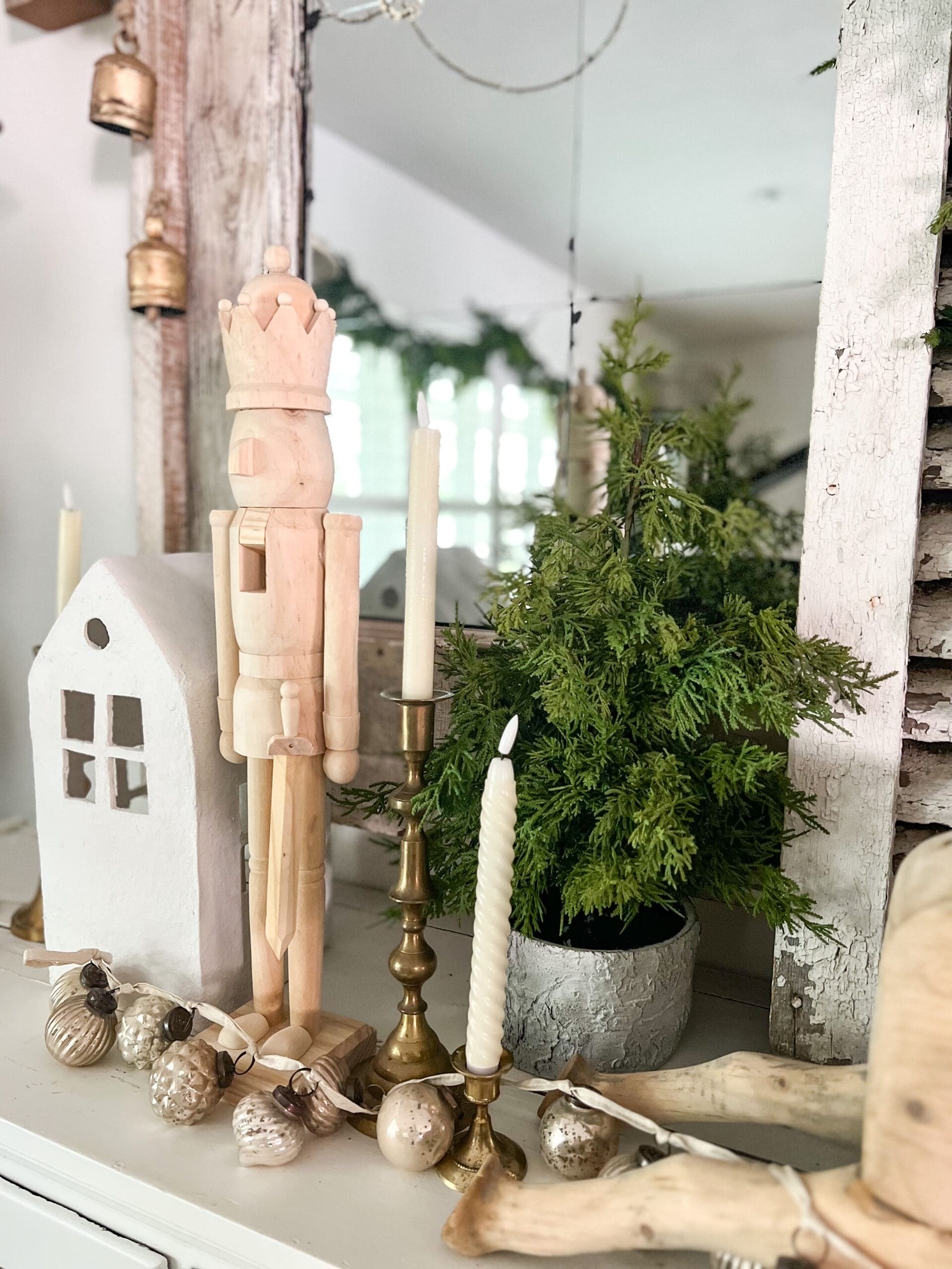 large wooden nutcracker next to a small white house and a little Christmas tree as well as golden candlesticks