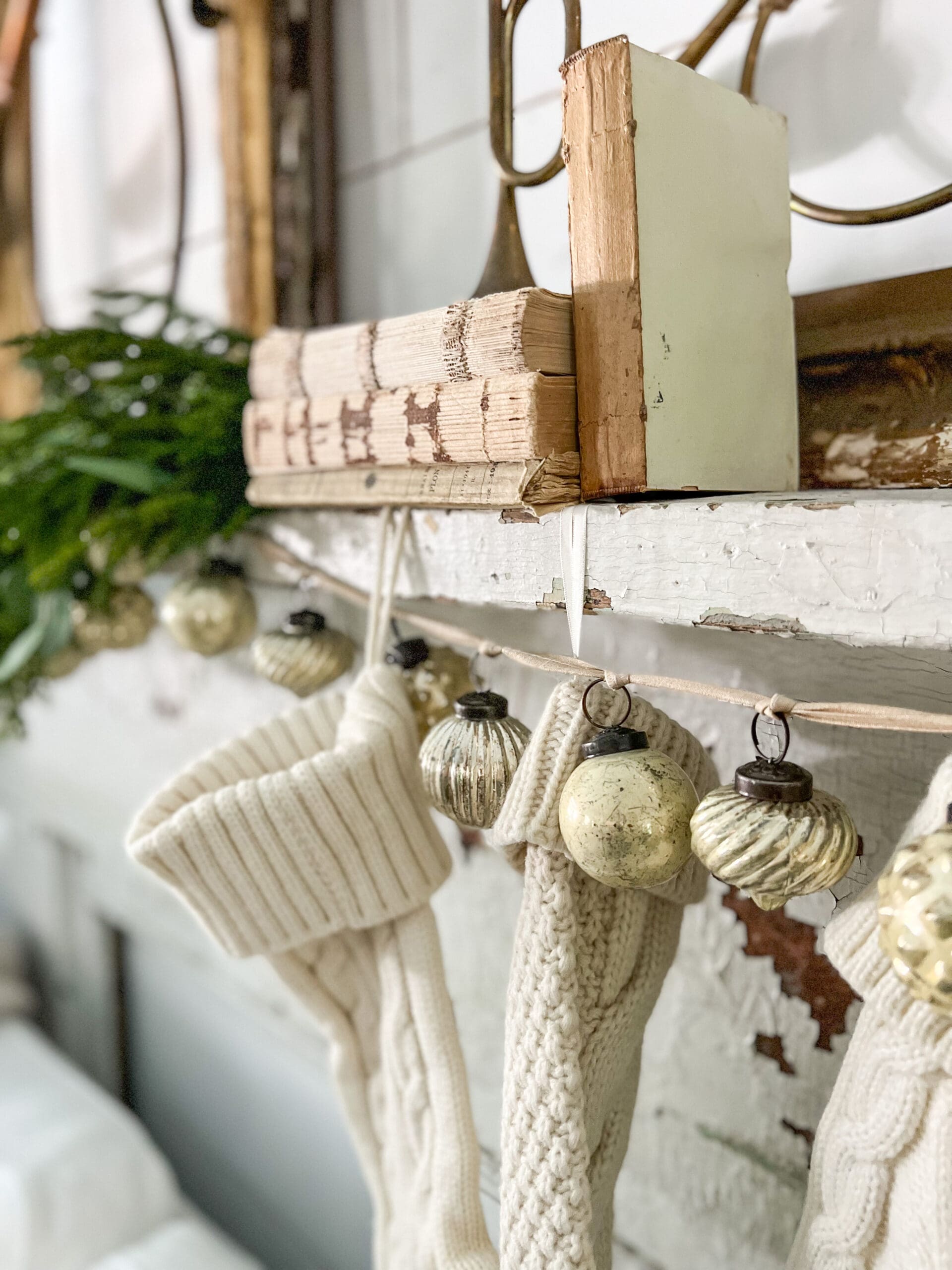 close up of white books on a mantel with stockings hung from it, also styled with an ornament garland