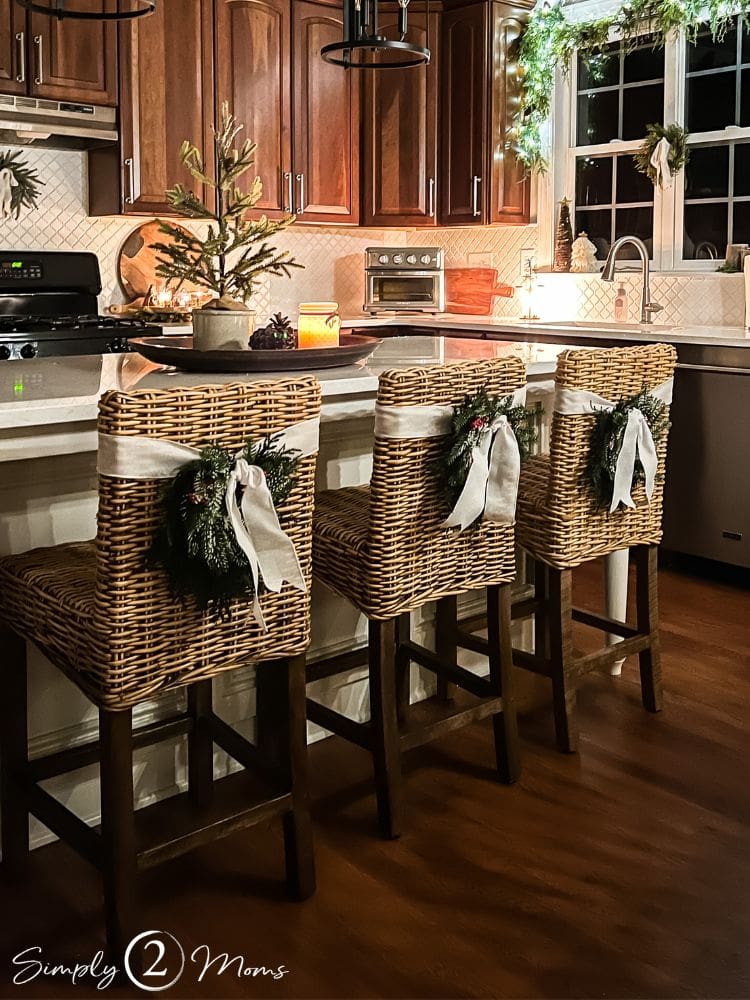small Christmas wreaths hung with ribbon on the back of kitchen barstools