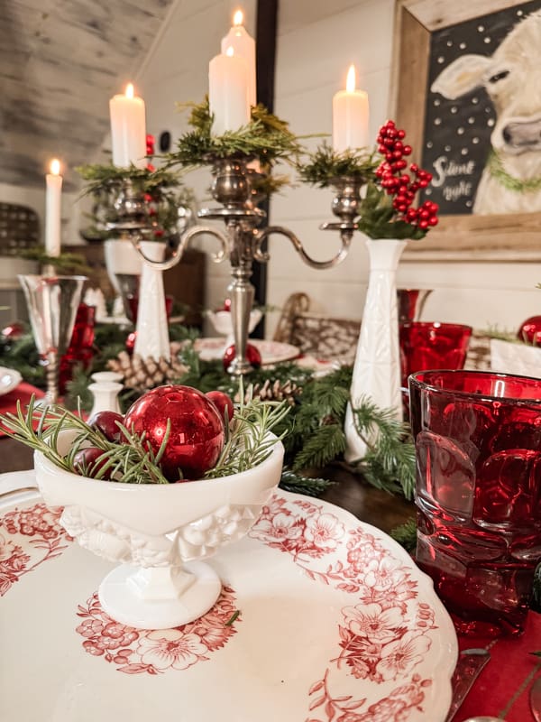 closeup of ironstone with red embellishments on a Christmas tablescape with candles going down the middle