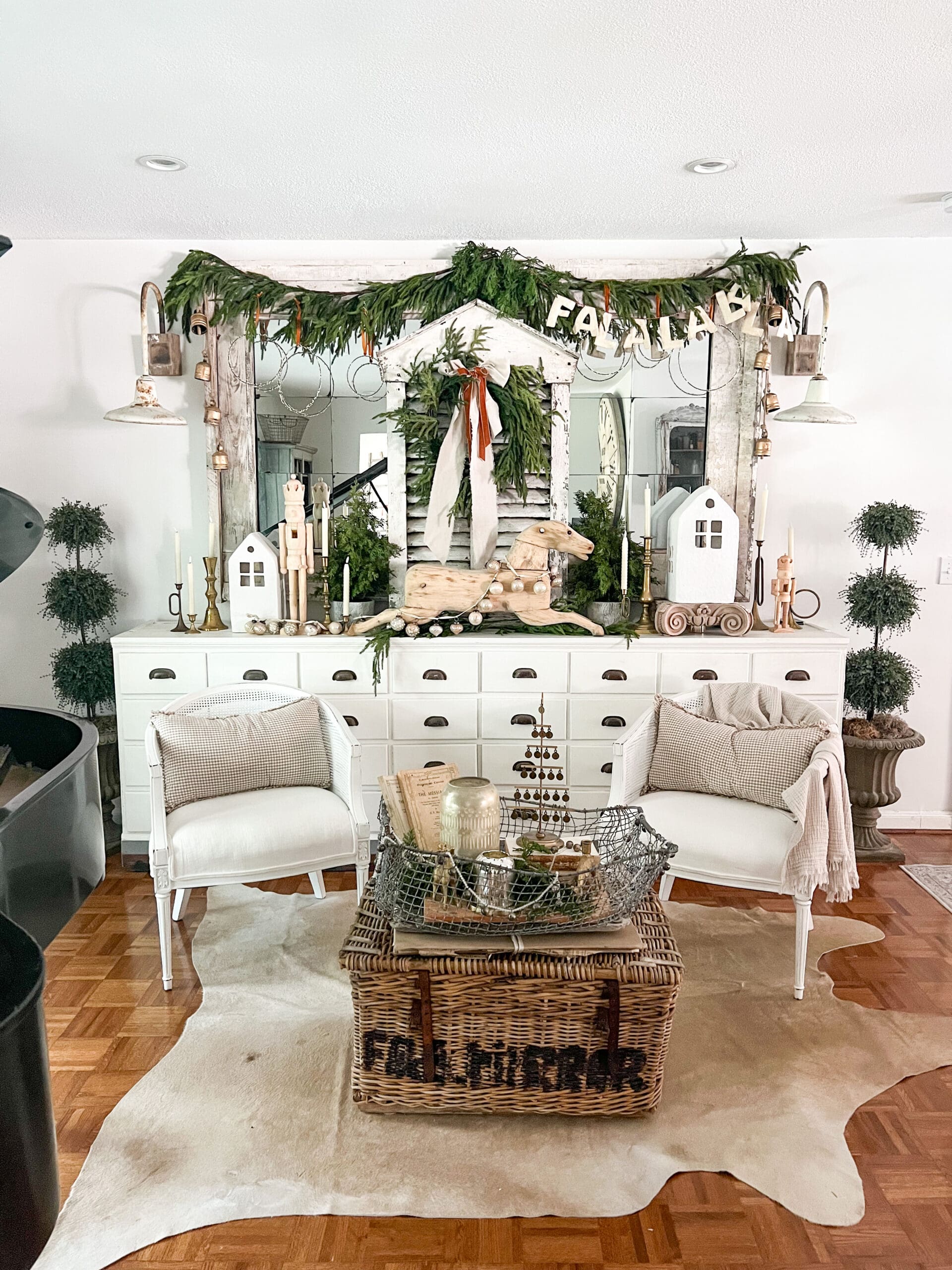 wide angle of an apothecary with a large white mirror on top styled with christmas greenery, a wooden rocking horse, and a large white window shutter